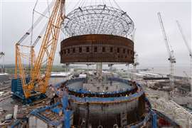 giant rusty steel ring lifted by yellow and blue Sarens SGC-250 giant ring crane